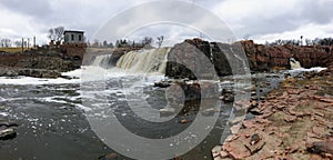 The Big Sioux River flows over rocks in Sioux Falls South Dakota with views of wildlife, ruins, park paths, train track bridge, tr