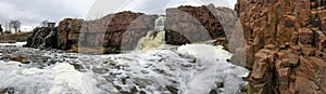 The Big Sioux River flows over rocks in Sioux Falls South Dakota with views of wildlife, ruins, park paths, train track bridge, tr