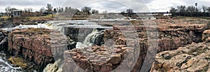 The Big Sioux River flows over rocks in Sioux Falls South Dakota with views of wildlife, ruins, park paths, train track bridge, tr