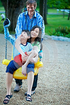 Big sister holding disabled brother on special needs swing at pl