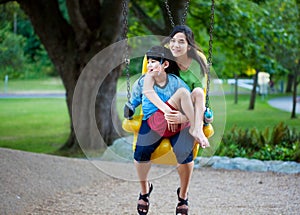 Big sister holding disabled brother on special needs swing at pl