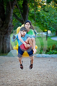 Big sister holding disabled brother on special needs swing at pl