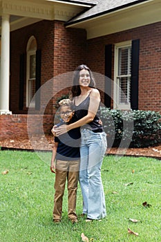 A big sister hugging on her little brother outside their home