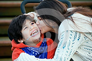 Big sister kissing disabled little brother in wheelchair