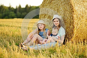 Big sisters and their baby brother having fun in a wheat field on a summer day. Children playing at hay bale field during harvest
