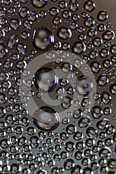 Big and small water drops on glass against dark background