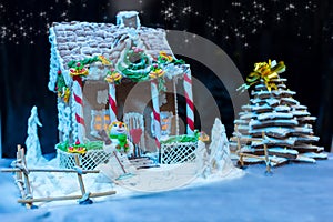 Big snow-covered homemade gingerbread house, gingerbread Christmas tree and a sugar mastic snowman at night