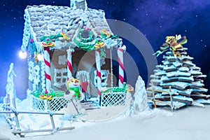 Big snow-covered homemade gingerbread house, gingerbread Christmas tree and a sugar mastic snowman at night