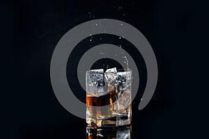 Whiskey splash from the fallen ice cube into glass with beverage isolated on black background