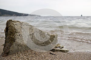 Big stone on the sea shore. Wet sand, transparent water. Overcast cloudy sky.