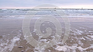 Big stormy waves in the sea. Beautiful seascape with pier, sandy beach at sunset.