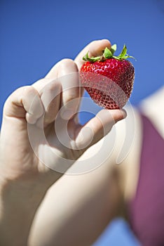 Big strawberry holding by woman in front of blue sky