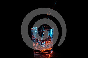 Big stream of water being poured into a square glass under blue and orange lights isolated on a black background