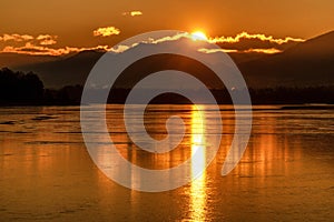 Big sun due sunrise over mountains. Reflcetion on frozen water surface on lake