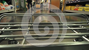 Big supermarket shopping cart in motion goes between blurred shelves