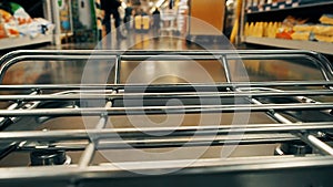 Big supermarket shopping cart in motion goes between blurred shelves. Color graded