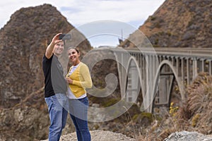 A young couple take a selfie in fron of the Big Creek Bridge, Big Sur, California, USA