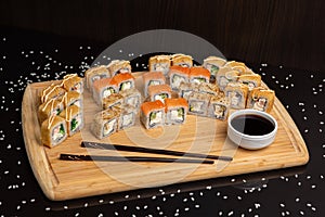 Big sushi set on light wooden dish isolated on black background