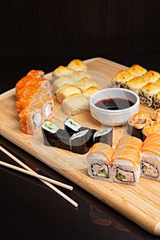 Big sushi set on light wooden dish isolated on black background