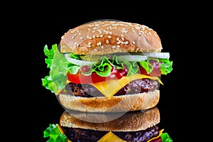 Big tasty hamburger or cheeseburger on black background with grilled meat, cheese, tomato, bacon, onion. Burger closeup