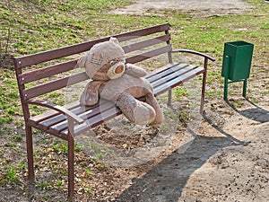 The big toy bear sitting on the bench alone. Loneliness concept