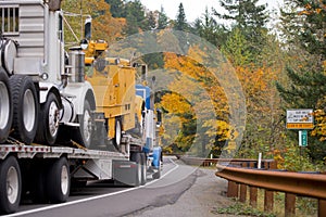 Big truck transports other trucks on flat bed trailer in yellow