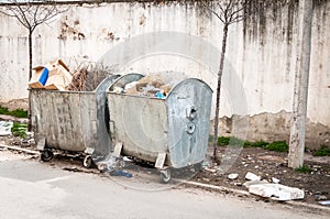 Big two metal dumpster garbage cans full of overflow litter polluting the street in the city