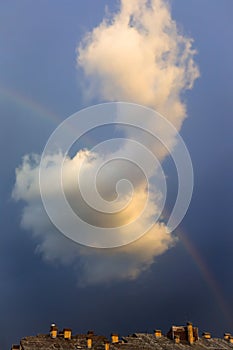 Big unusual cloud in the blue sky and a rainbow, bright light of sun set, and building sky after the rain vertical image
