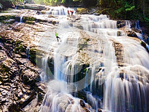 Big waterfall in the green tropical forest, with man climbing between the waterfall