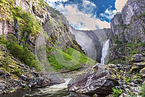 Big waterfall in the mountains, blue sky, green grass, summer