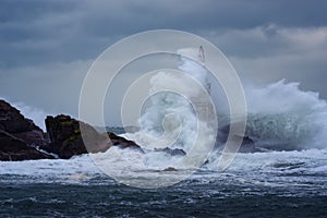 Big wave against old Lighthouse in the port of Ahtopol, Black Sea, Bulgaria on a moody stormy day. Danger, dramatic scene.