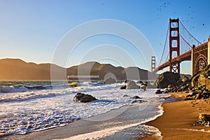 Big wave crashing into shore as water recedes from beach with Golden Gate Bridge