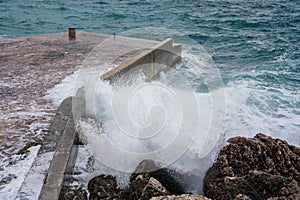Big wave splash on pier. Big sea wave on a windy day. Waves crash against concrete breakwater at port entrance. Giant waves