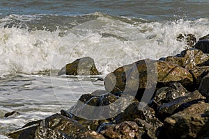 Big waves beat against a stone shore on an autumn day. Boulders by the sea against the backdrop of a stormy ocean. Cliffs in the