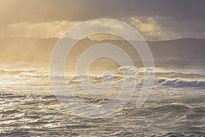 Big waves break on the coast, in the sunlit sea, passing through the clouds at sunset. Galicia, Spain