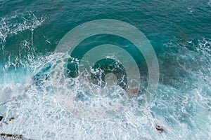 Big waves breaking on the shore. Waves and white foam. Coastal stones. View from above. The marine background is green