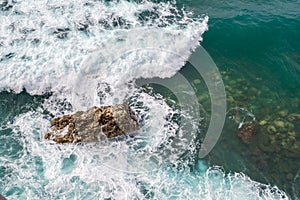 Big waves breaking on the shore. Waves and white foam. Coastal stones. View from above. The marine background is green