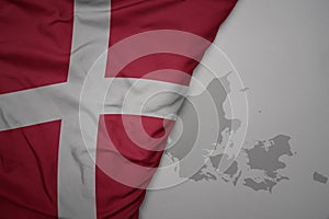 big waving national colorful flag and map of denmark on the gray background