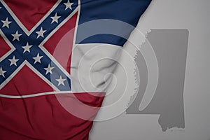 big waving national colorful flag and map of mississippi state on the gray background