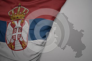 big waving national colorful flag and map of serbia on the gray background