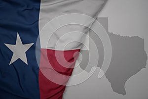 big waving national colorful flag and map of texas state on the gray background