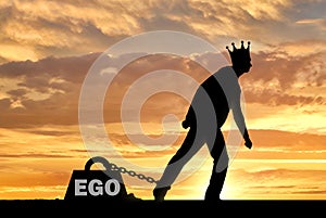 A big weight in the form of an ego is chained to the foot of a selfish and narcissistic man with a crown on his head photo