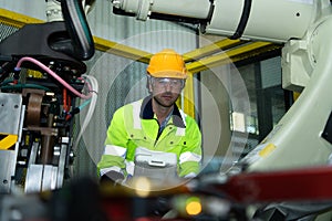 A big welding robot is being inspected and controlled by a robotics engineer.