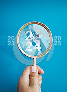 The big white 2024 year number with target icon inside the gold magnifying glass holding by hand.