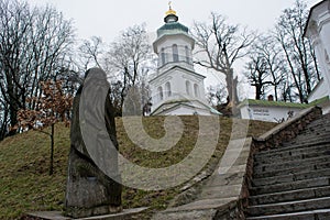 Big white ancient christian church with crosses, green roof and wooden idol near stairs