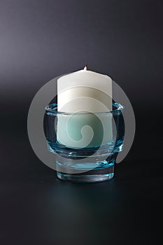 Big white candle in a blue transparent candlestick, against a dark background.