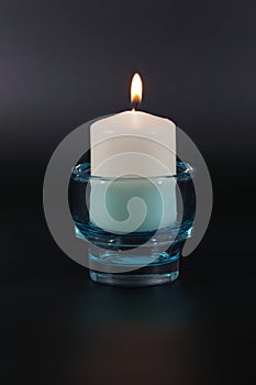 Big white candle in a blue transparent candlestick, against a dark background.