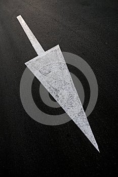Big white diagonal arrow sign, painted on black asphalt road, road signage example.