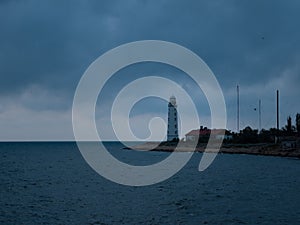 Big white lighthouse on the sea shore against the background of the cloudy evening sky.