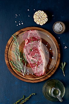 Big whole piece of raw beef meat, striploin on a wooden cutting board on dark blue background. Seasoning steak with salt, vertical